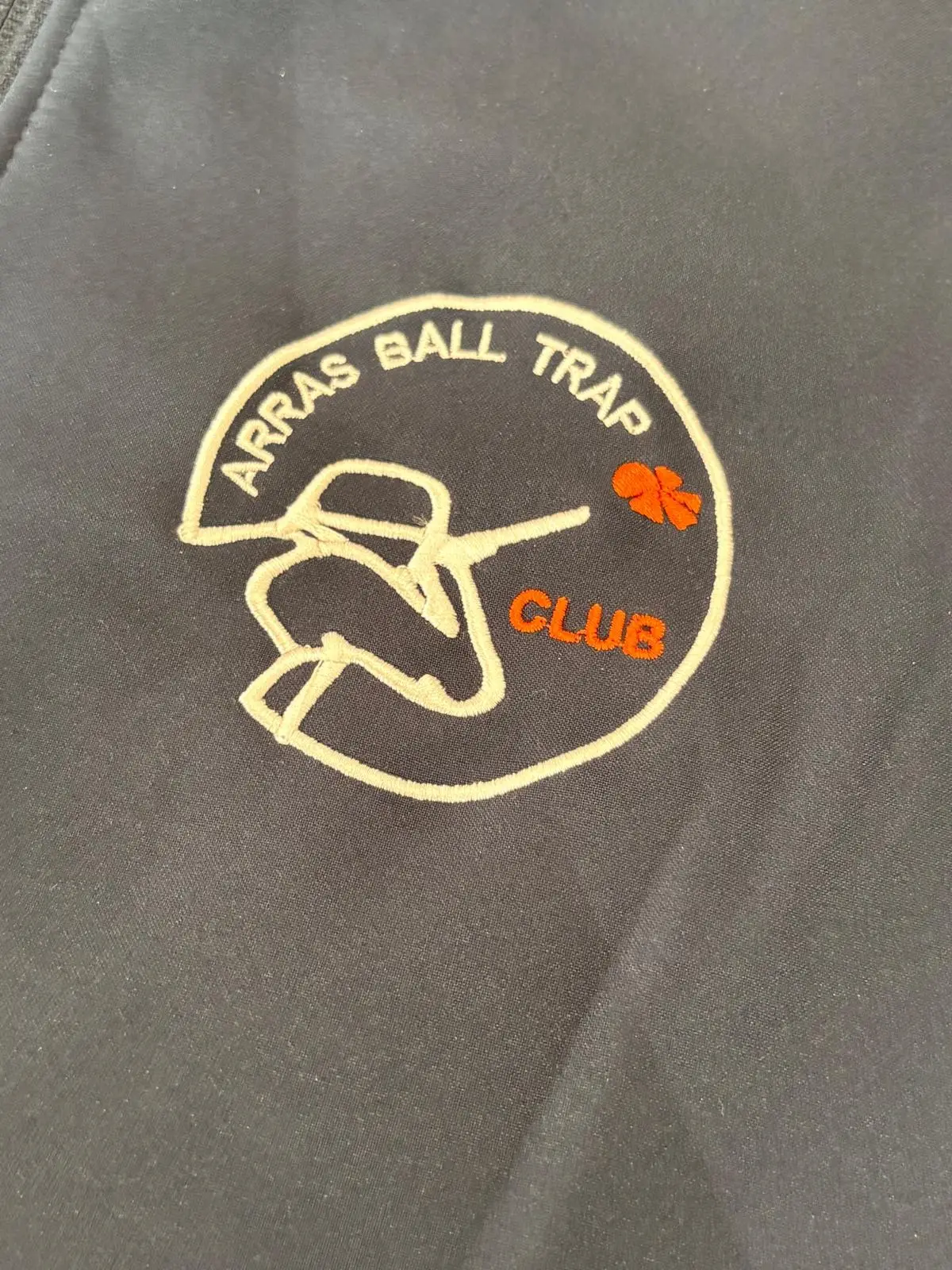 Gros plan sur le logo Arras Ball Trap Club brodé en blanc et orange