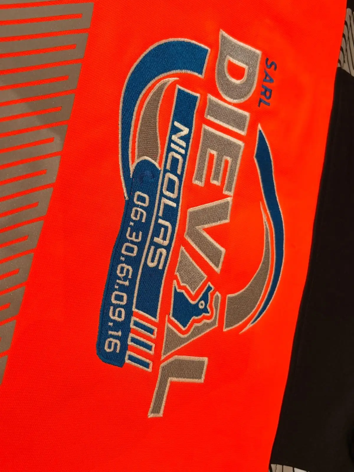 Logo SARL Dieval Nicolas brodé en bleu, gris et blanc avec numéro de téléphone sur un vêtement de travail orange