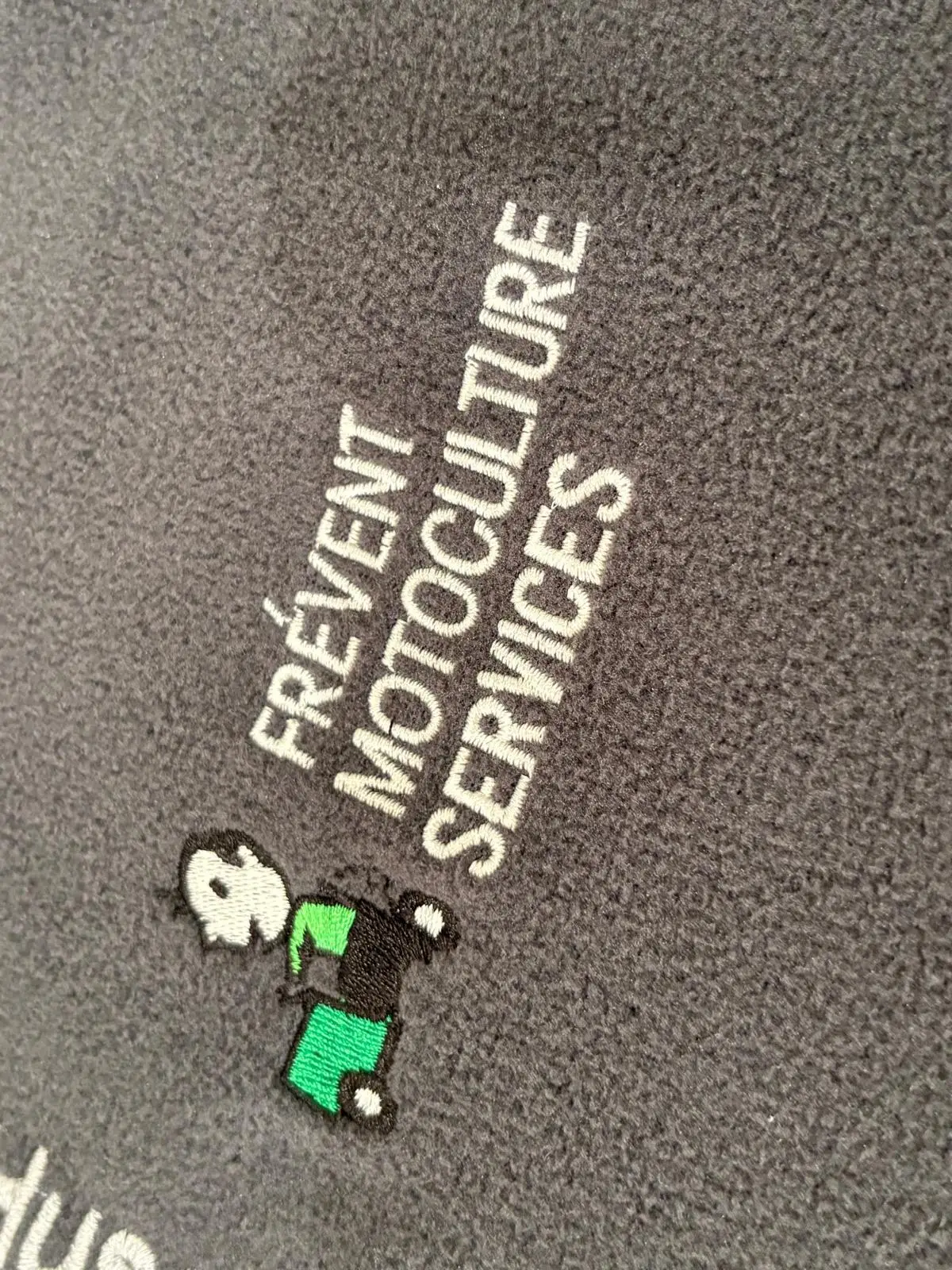 « Frévent Motoculture Services » brodé en blanc avec un petit motif de tondeuse sur une polaire grise