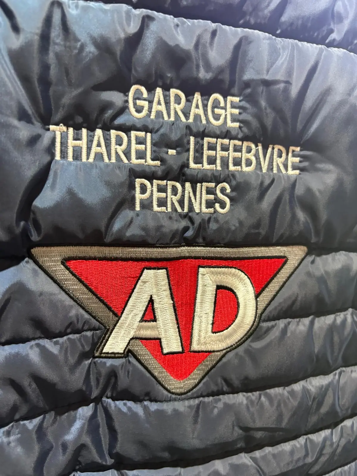 « Garage Tharel-Lefebvre Pernes » et logo AD rouge et blanc brodés dans le dos d'une doudoune bleu marine