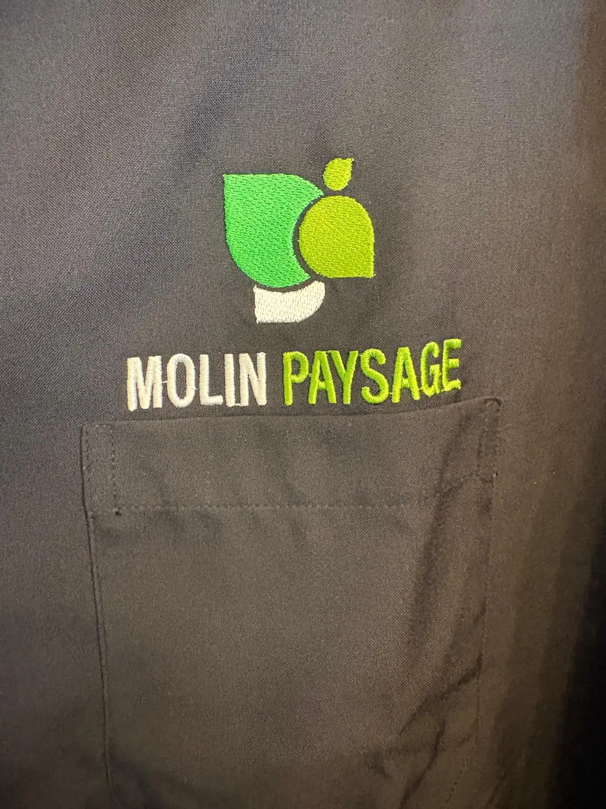 Logo Molin Paysage brodé en vert et blanc sur la poitrine d'une veste de travail