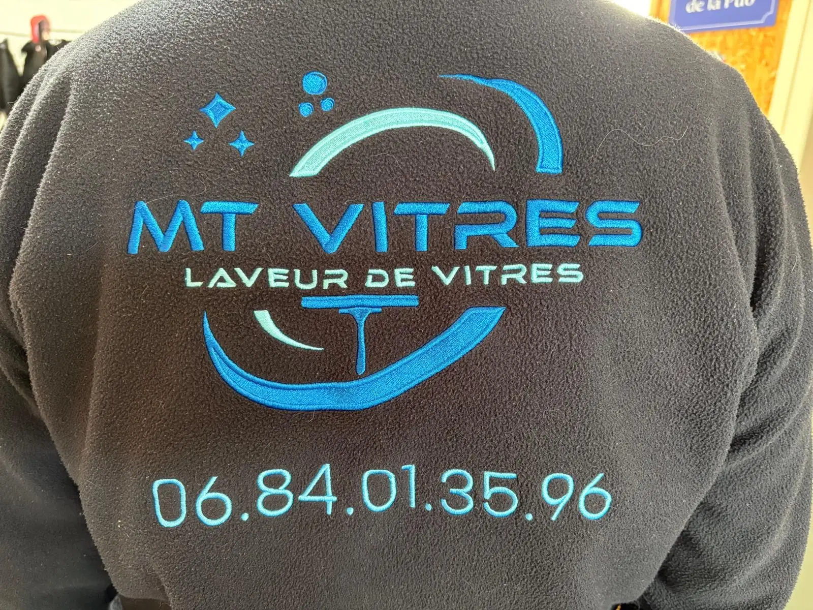 Logo MT Vitres laveur de vitres et numéro de téléphone brodés en bleu dans le dos d'une polaire noire