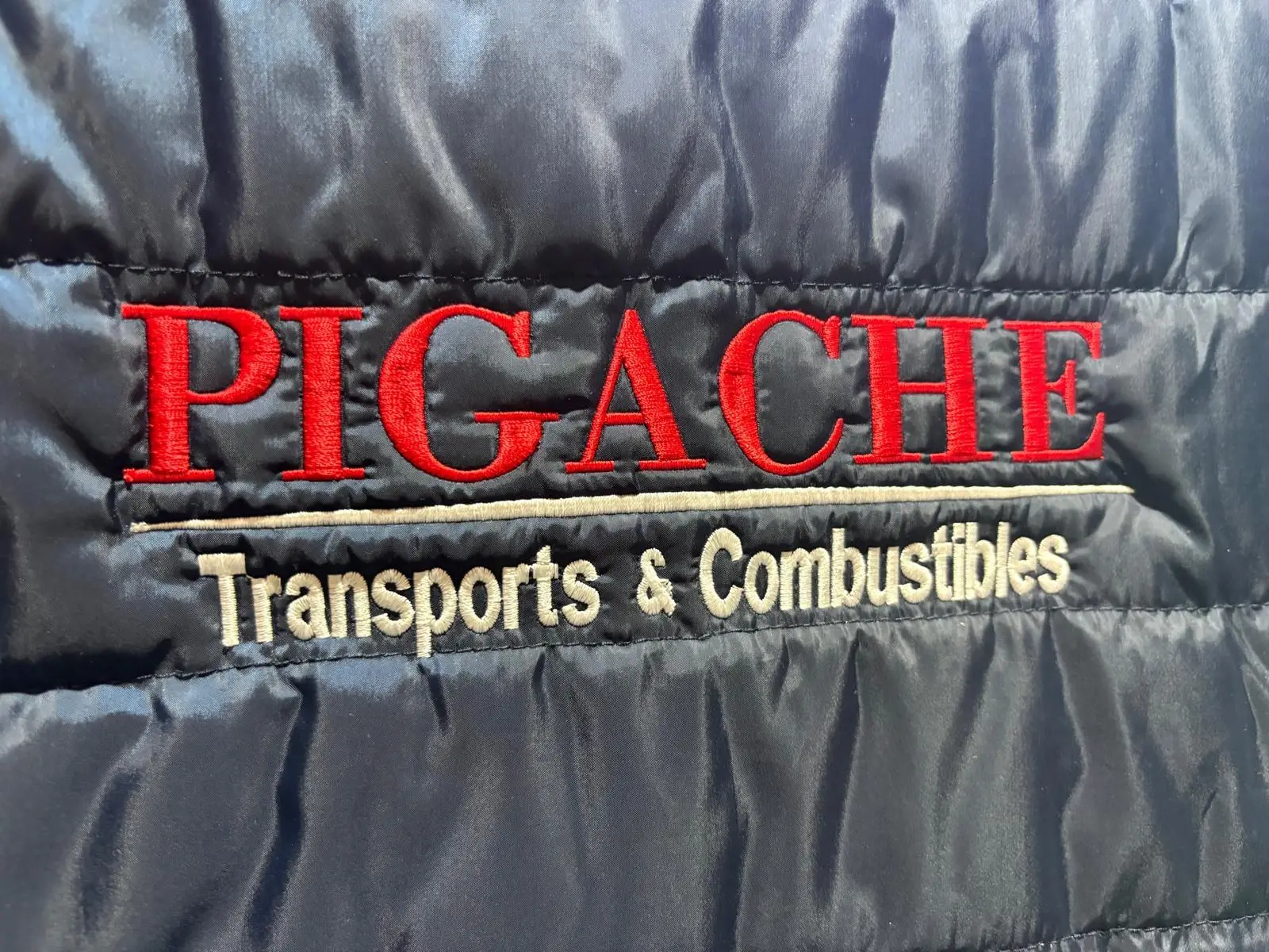 Inscription « Pigache Transports & Combustibles » brodée en rouge et blanc sur une doudoune bleu marine