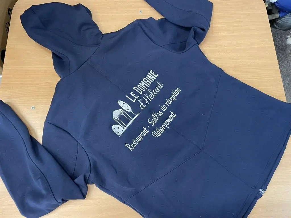 Logo d'un restaurant brodé en blanc sur un sweat à capuche bleu marine