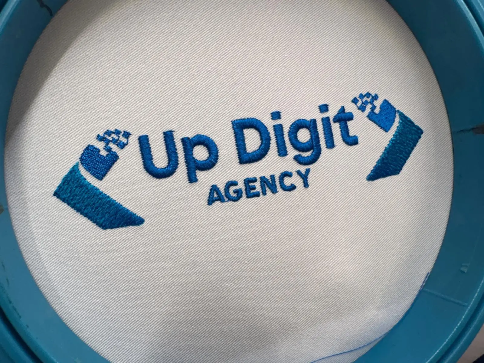 Logo Up Digit Agency brodé en bleu foncé et bleu clair sur le devant d'une casquette blanche, dans le cadre de la brodeuse